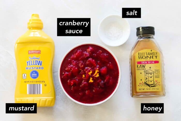 bottle of yellow mustard, white bowl of cranberry sauce, small bowl of salt, and a bottle of honey on a white counter with text overlay