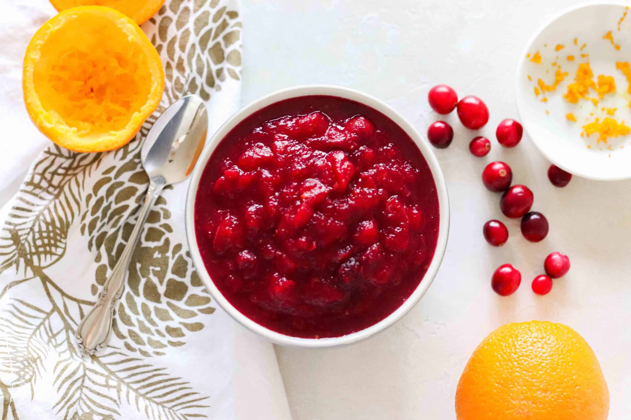 white and gold napkin with a white bowl of cranberry sauce with oranges and fresh cranberries on counter