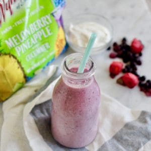 Melon Berry Pineapple with Cucumber Smoothie in glass with blue straw on white and blue napkin with Wyman's frozen fruit and yogurt in background