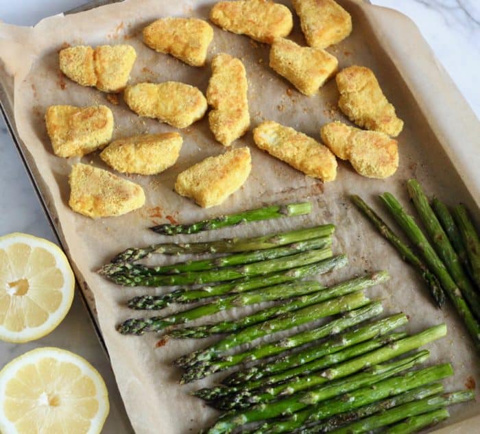baking sheet of cooked fish sticks and roasted asparagus with lemons