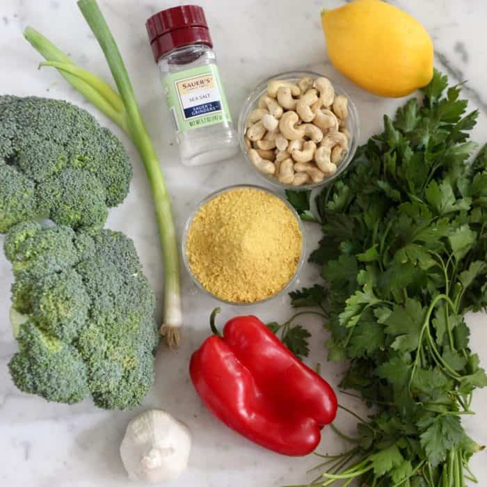 ingredients for vegan broccoli salad of fresh broccoli, green onion, garlic, salt, nutritional yeast, red bell pepper, cashews, lemon, and parsley