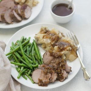 pork tenderloin, green beans, mashed potatoes, gravy on white plate with fork and tan napkin