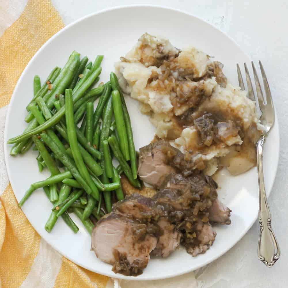 green beans, pork tenderloin with gravy, mashed potatoes and fork on white plate with white and yellow towel