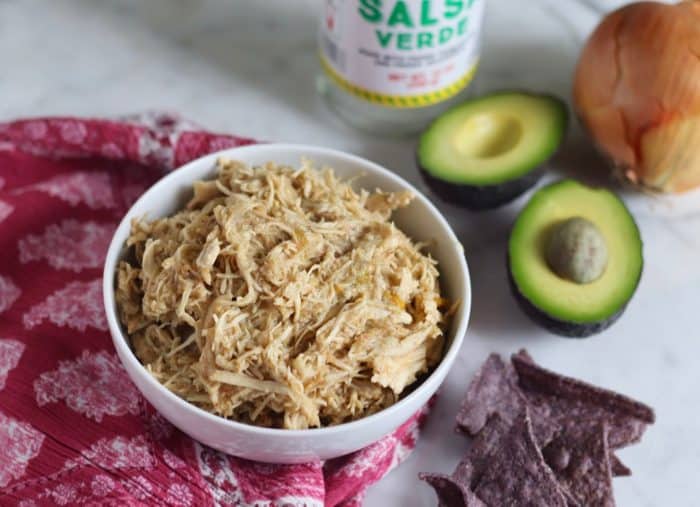 bowl of salsa chicken with halved avocado, tortilla chips, empty salsa verde jar