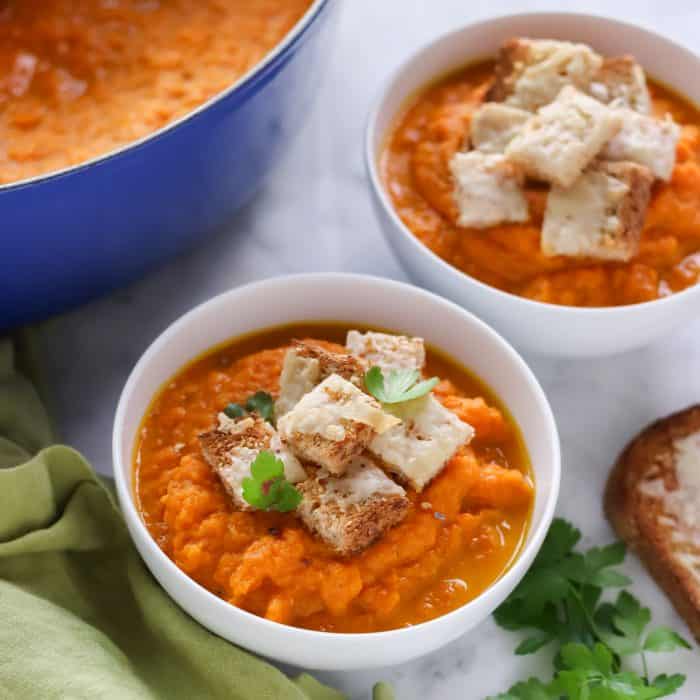 bowls of roasted carrot soup topped with parsley and cheese croutons 