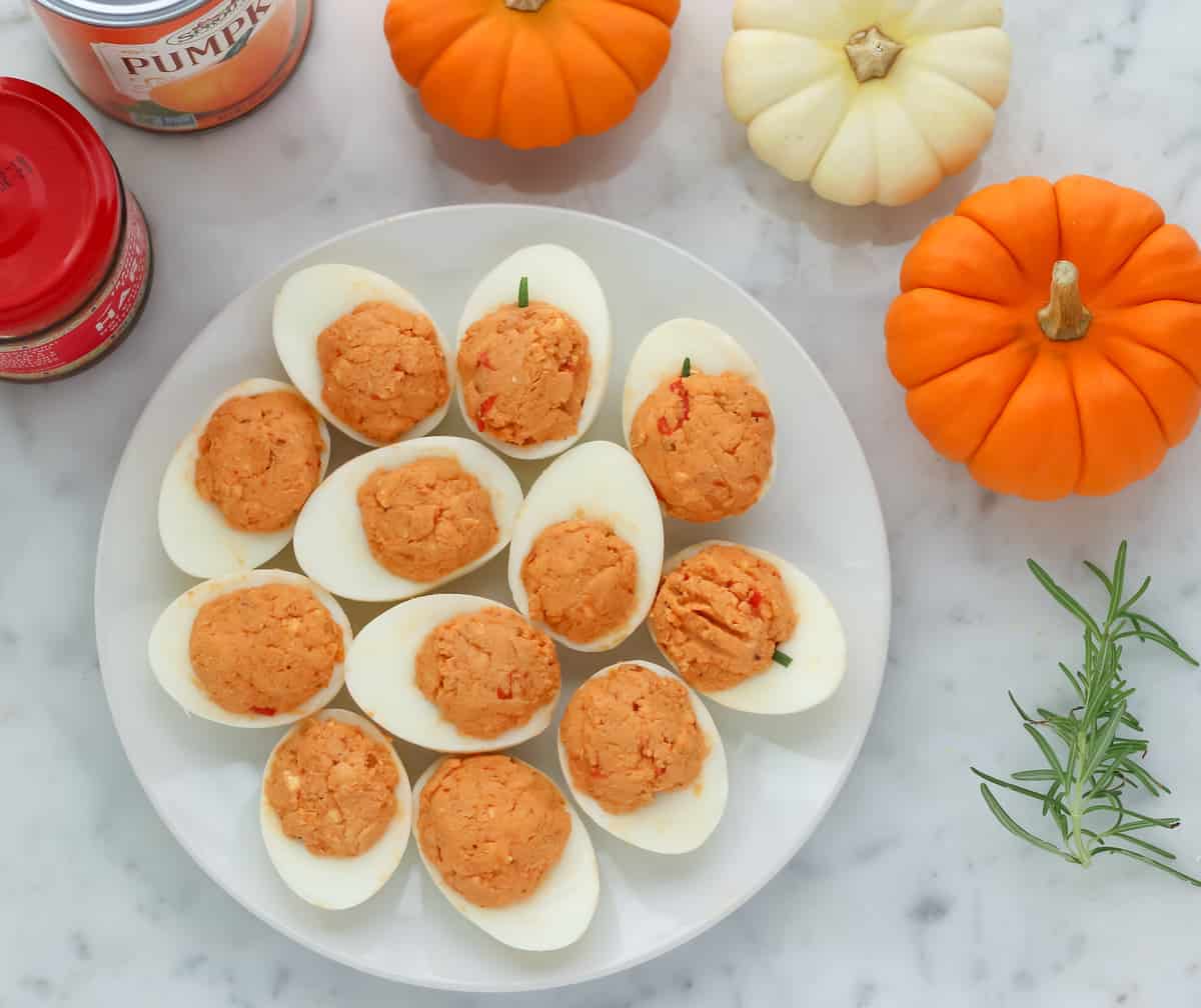 deviled eggs on white plate next to mini pumpkins on marble counter