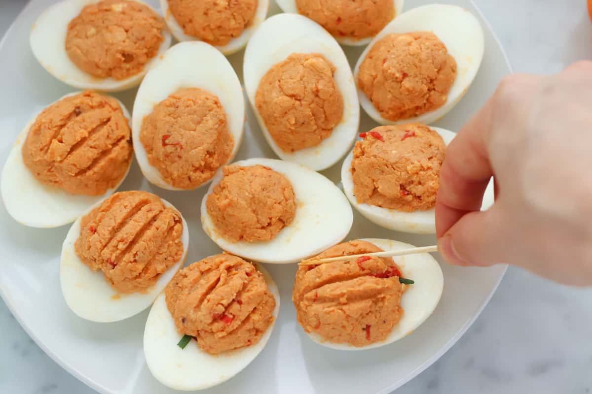 hand holding a toothpick pressing into orange deviled eggs