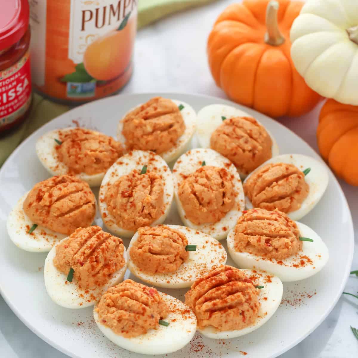 plate of paprika sprinkled deviled eggs with small pumpkins and a can of pumpkin and harissa paste