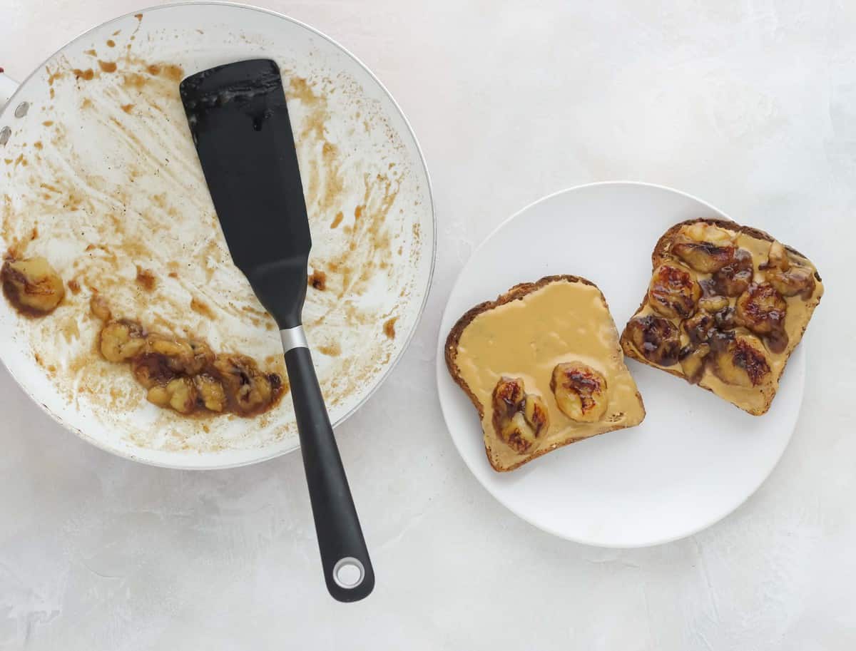 skillet with bananas in sauce with spatula, plate of peanut butter toast