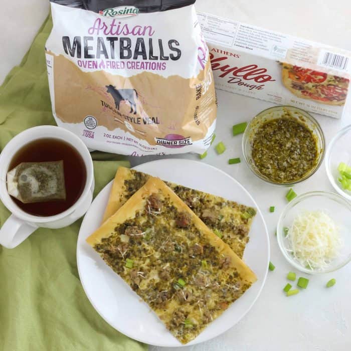 flatbreads stacked on a white plate and green napkin with tea, meatballs, phyllo dough, pesto, parmesan, green onions