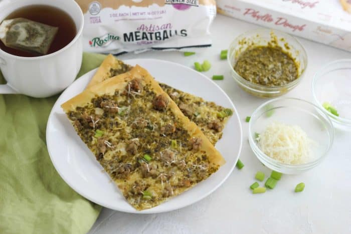 white plate of flatbreads with green onions sprinkled and meatballs, pesto, parmesan