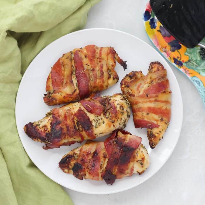 bacon wrapped chicken breast on white plate with spatula and green napkin