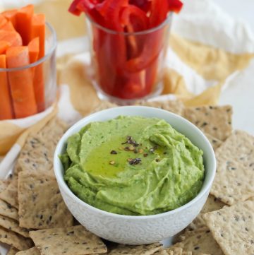 white bowl of spinach hummus surrounded by crackers, sliced veggies