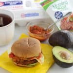 breakfast burger on yellow napkin, avocado, tea, salsa, egg carton, veggie burger wrapper