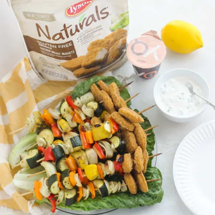 chicken nugget vegetable kabobs on a plate of green leaf lettuce, dipping sauce, lemon, yogurt, bag of frozen chicken nuggets