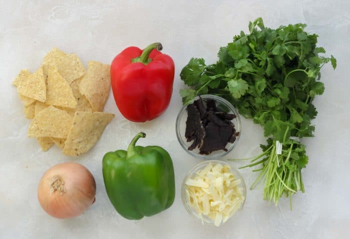 tortilla chips, onion, red bell pepper, green bell pepper, bowl of beef jerky, bowl of shredded cheddar cheese, cilantro