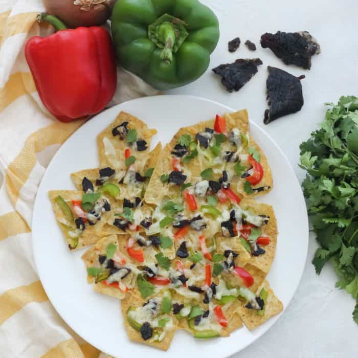 white plate with beef jerky nachos, red and green bell pepper, beef jerky, cilantro