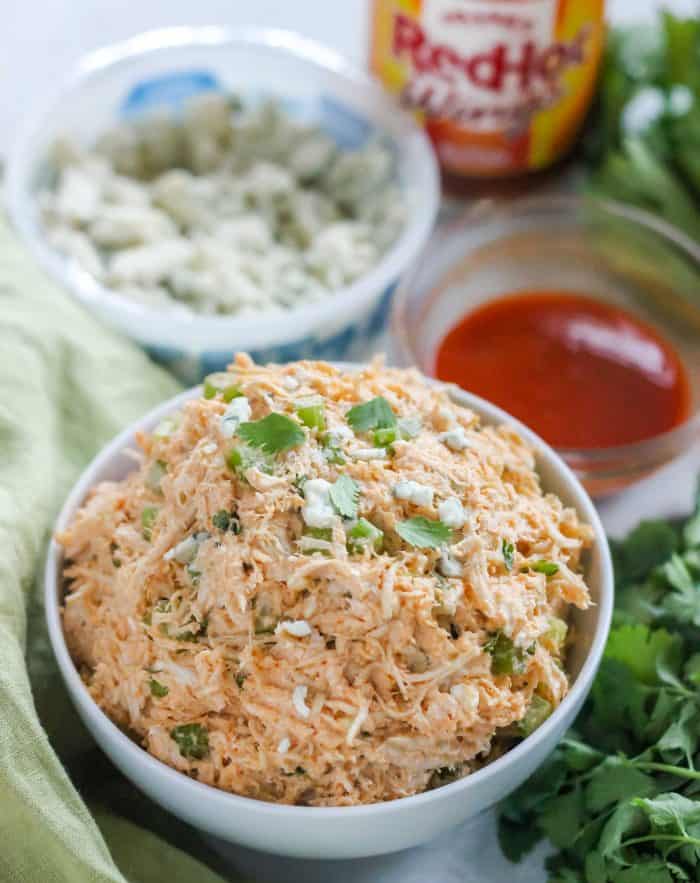 white bowl of Buffalo Chicken Salad topped with cilantro, wing sauce, blue cheese, celery