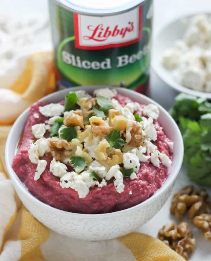 bowl of beet hummus topped with walnuts, cilantro, feta, and can of beets