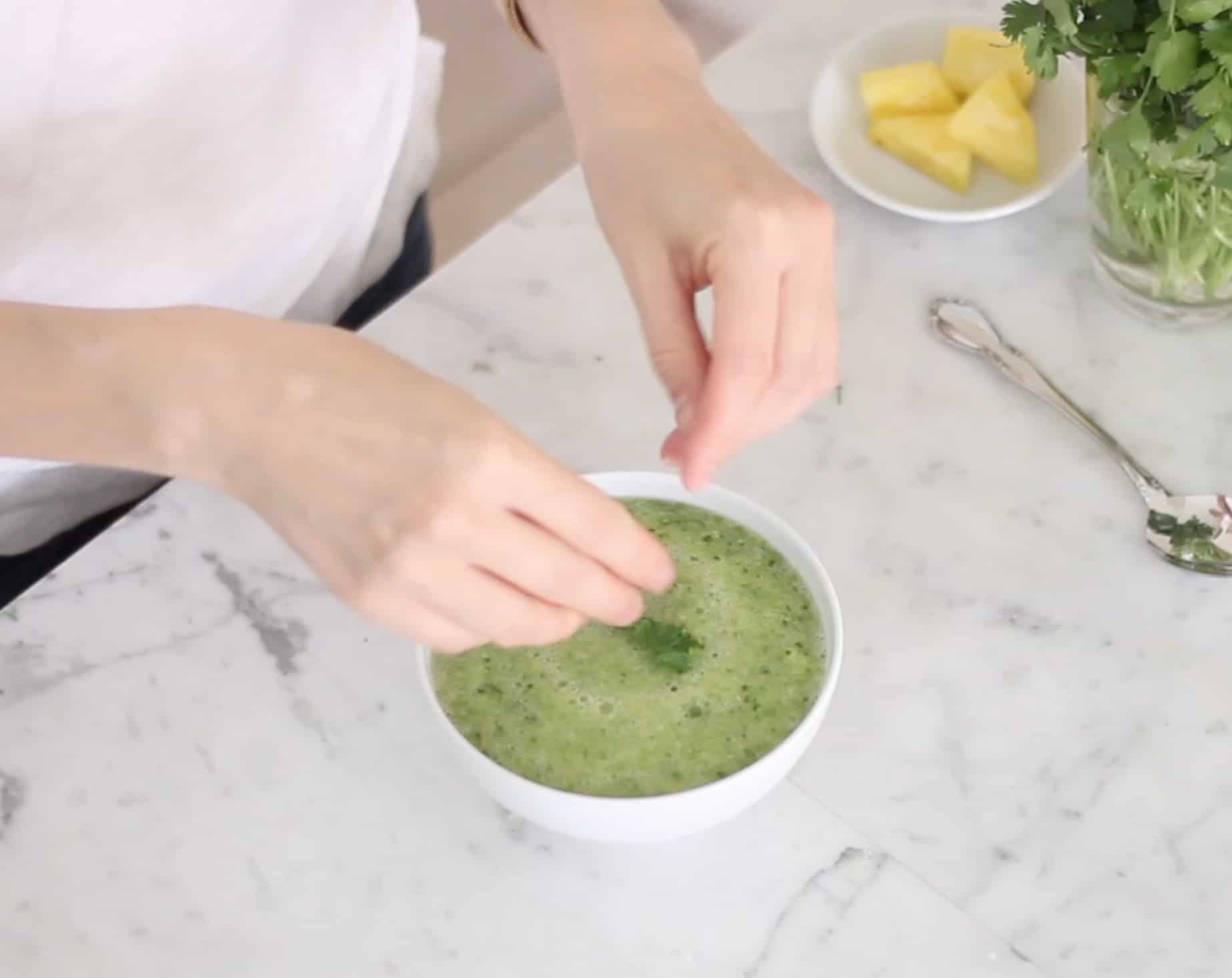 hands sprinkling cilantro into bowl of pineapple cucumber gazpacho