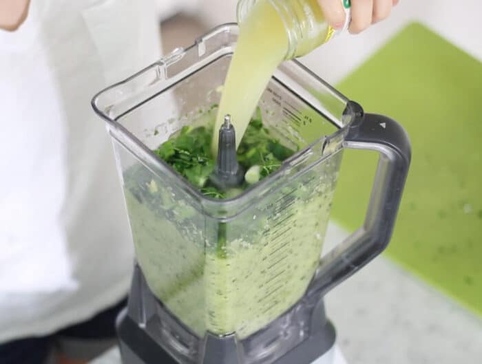 hand pouring pineapple juice into blender with cucumber gazpacho