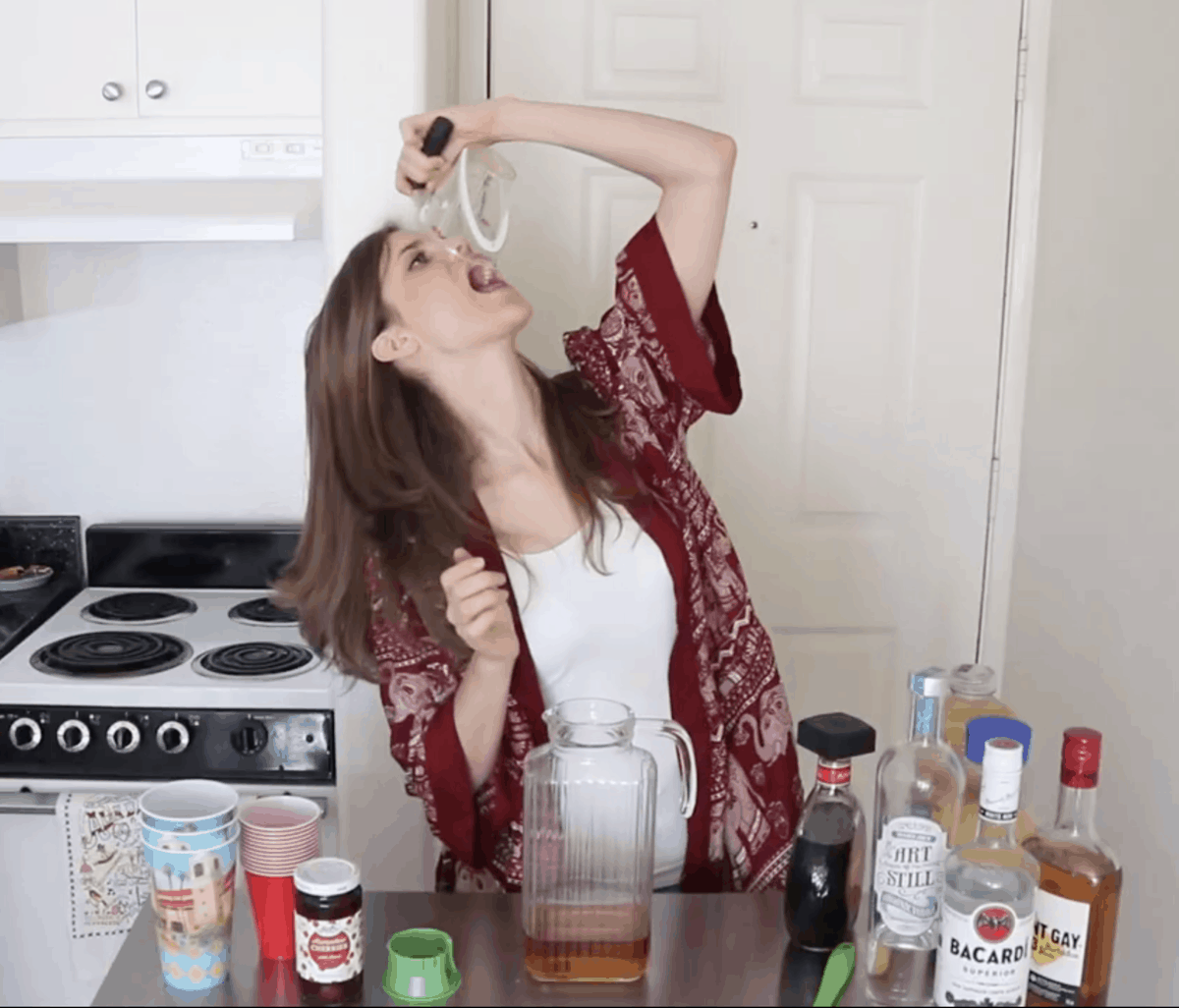 brunette drinking from a measuring cup while mixing a cocktail