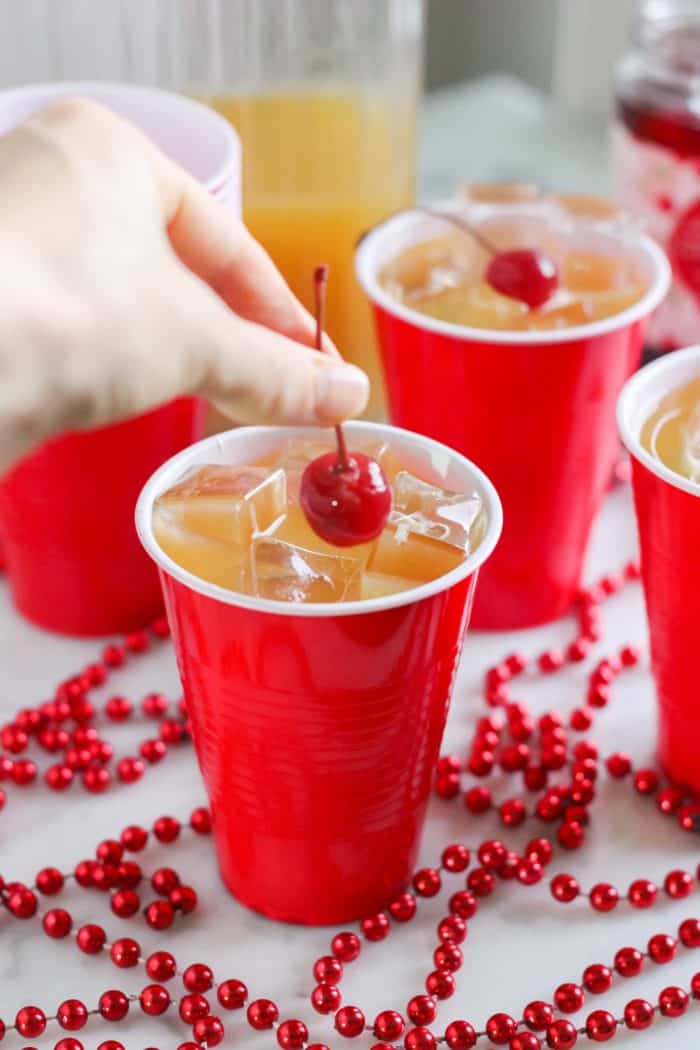 hand placing cherry into yellow hammer drink with drink and pitcher in background