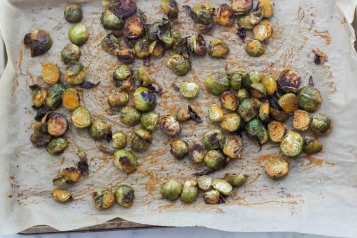 parchment lined baking sheet with roasted Brussels sprouts covered in buffalo-butter sauce