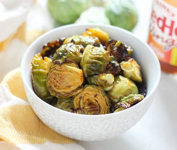 white bowl of buffalo Brussels sprouts with white and yellow striped dish towel