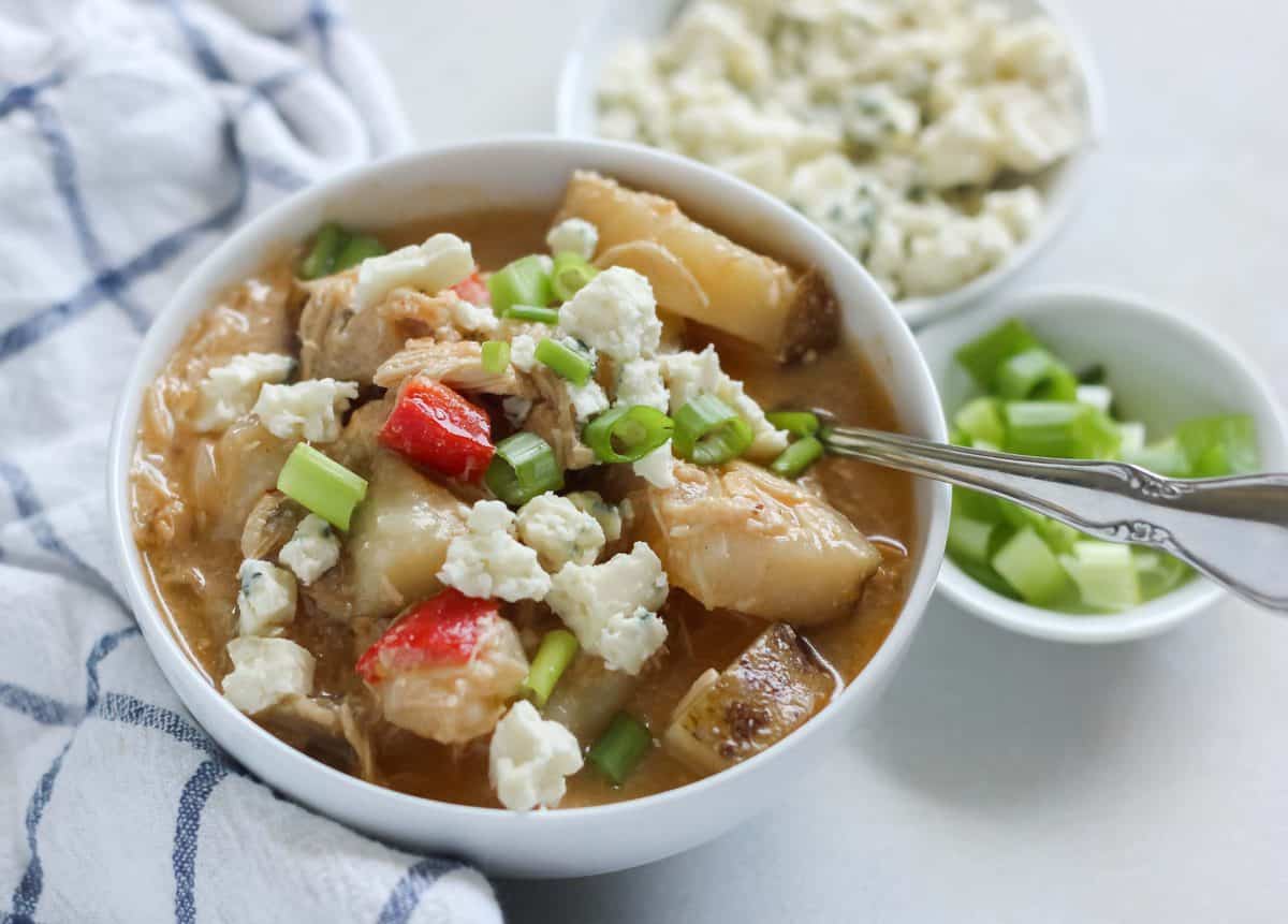 spoon in a white bowl of buffalo chicken chowder topped with blue cheese and green onion, blue and white striped napkin