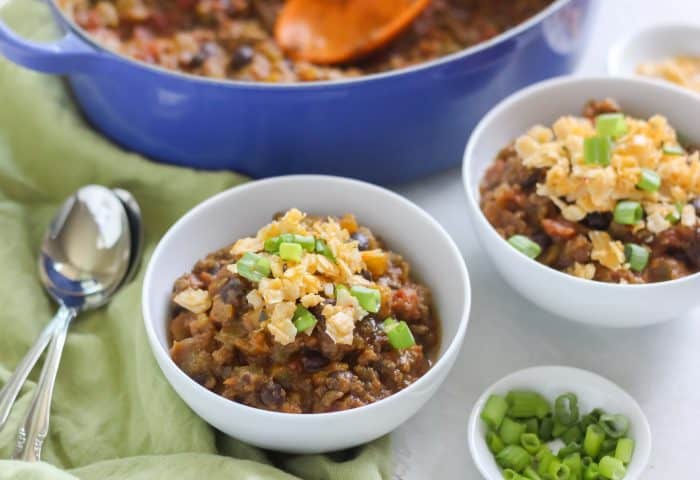 green napkin with white bowls of pumpkin chili topped with green onion and cheddar