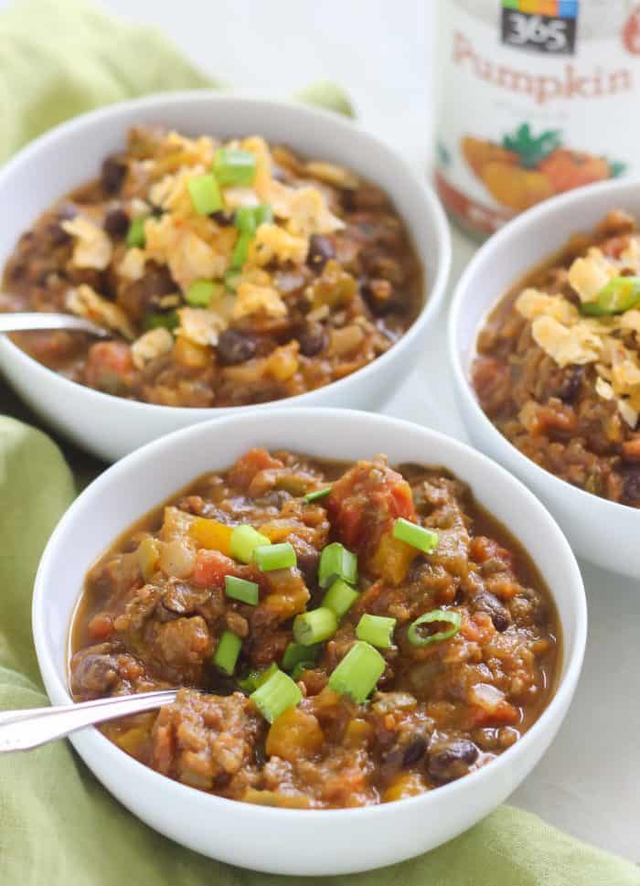 three bowls of chili with spoons, topped with green onions, some topped with cheese, can of pumpkin