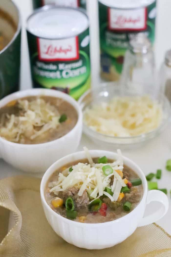 white bowl of cheeseburger soup on gold napkin with green onions and shredded cheese