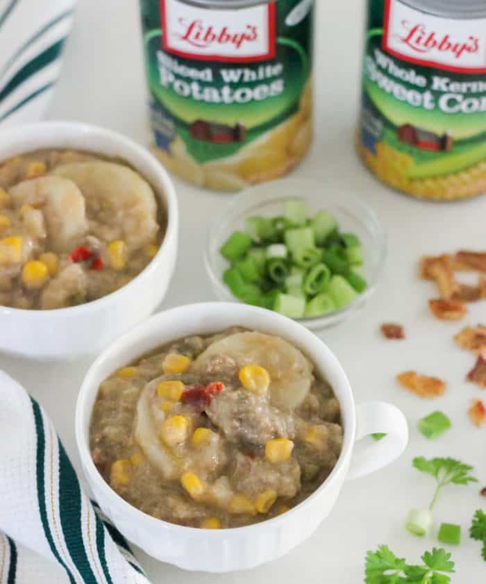 cheeseburger chowder in white cups with green and white napkin and bacon bits, green onions, canned veggies