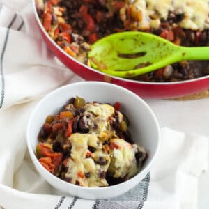 bean casserole in a white bowl on white napkin with skillet and spoon in background