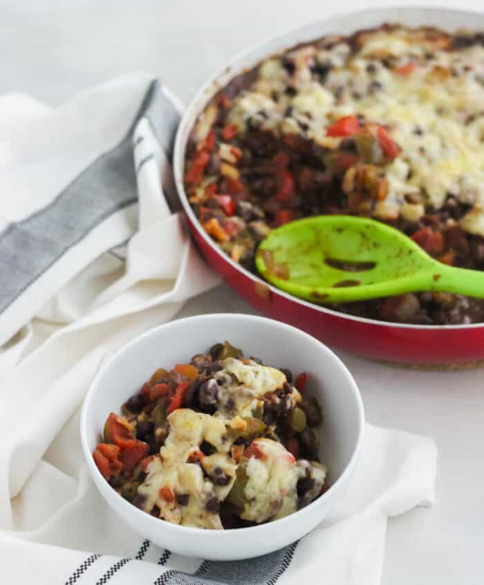 red skillet and white bowl with bean casserole on white and black napkin