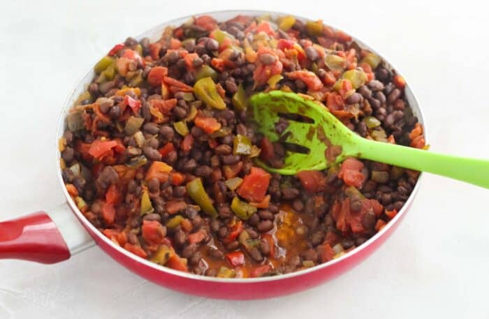 beans and veggies stirred in a red skillet with a green spoon