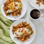 white countertop with green napkin and two plates of sweet potato bacon hash topped with fried eggs and a mug of tea with plate of bacon crumbles