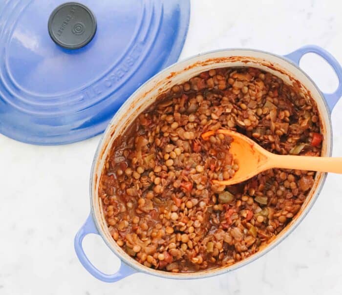 blue pot on white counter with top filled with chili and an orange spoon