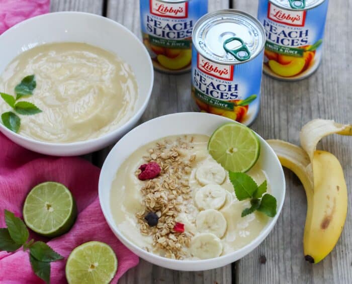 white bowls filled smoothies topped with granola, banana, lime, mint and whole banana with canned peaches