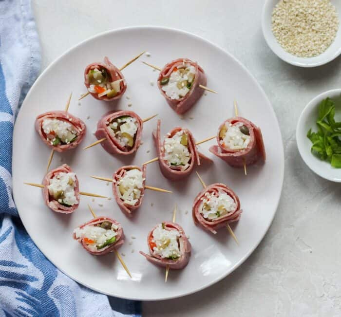 white table with blue napkin and white plate filled with sushi made with beef plus two small bowls of celery leaves and sesame seeds