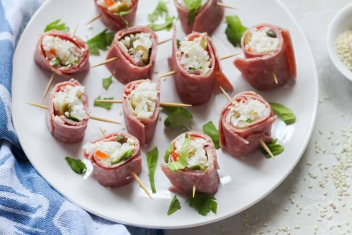 white plate of beef sushi sprinkled with sesame seeds and celery leaves