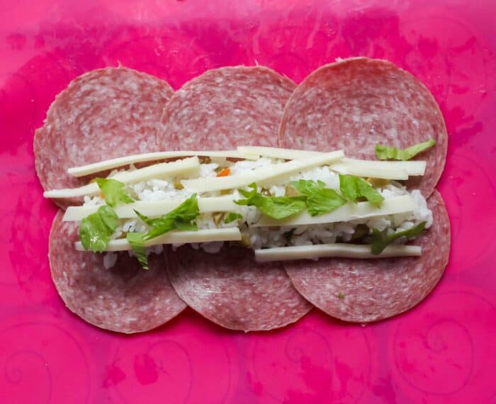 beef salami on a pink baking liner topped with rice, cheese, and celery leaves