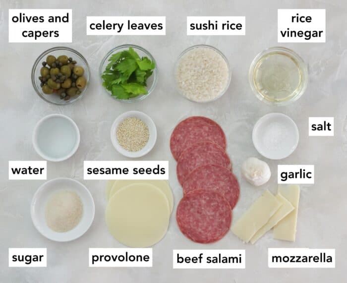 white counter with ingredients and words that say capers, olives, celery leaves, sushi rice, rice vinegar, salt, garlic, mozzarella, beef salami, provolone, sesame seeds, sugar and water
