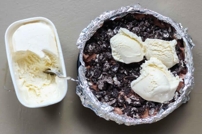 carton of vanilla ice cream next to a foil-lined springform pan filled with oreos and ice cream