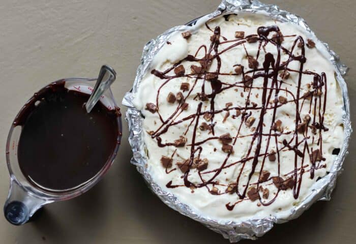 cup of chocolate sauce next to a springform pan filled with ice cream pie