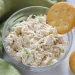 chicken salad and a ritz cracker in a glass bowl on white table with green napkin