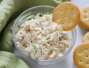 chicken salad and a ritz cracker in a glass bowl on white table with green napkin
