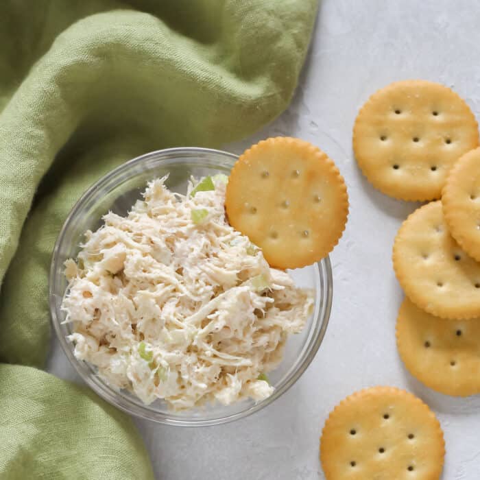 white table with green napkin and a glass bowl of chicken salad with ritz crackers