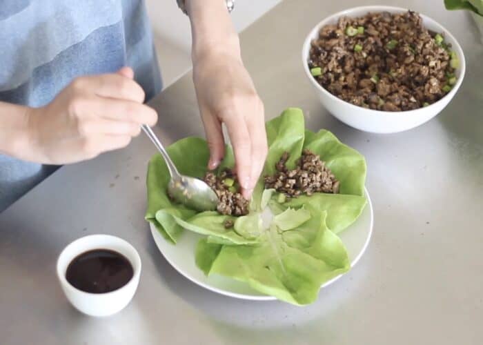 hand and spoon filling lettuce leaves with ground turkey and mushrooms